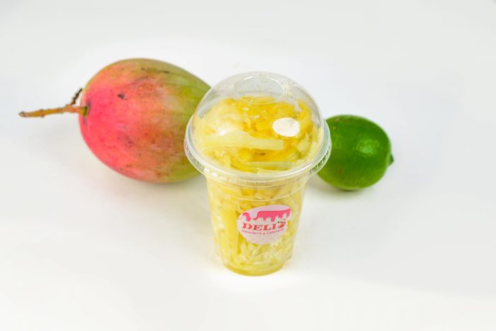 Mango picado en vaso de Deli's junto a un mango y un limón