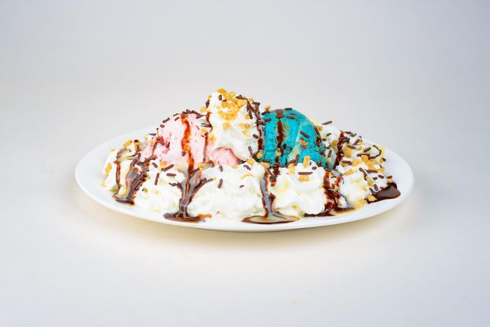 Plato de helado rosado y azul con crema batida, maní y chocolate